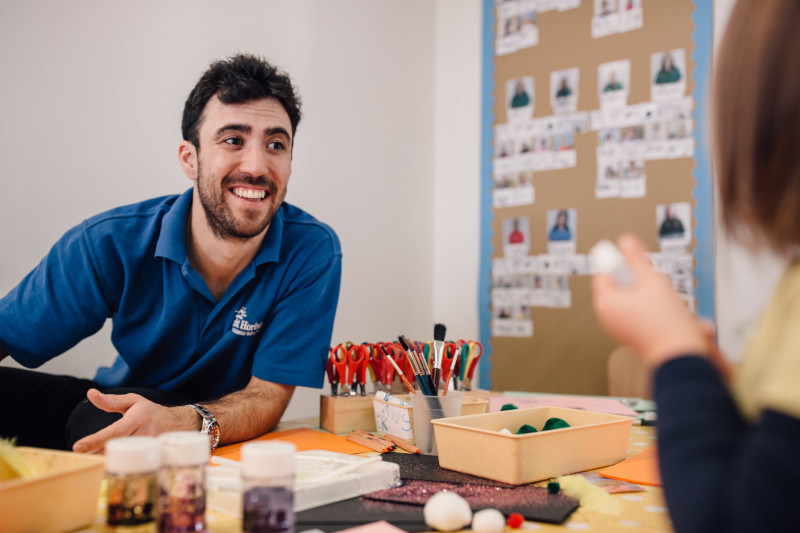 A male nursery worker smiling at a child who is mostly off-camera