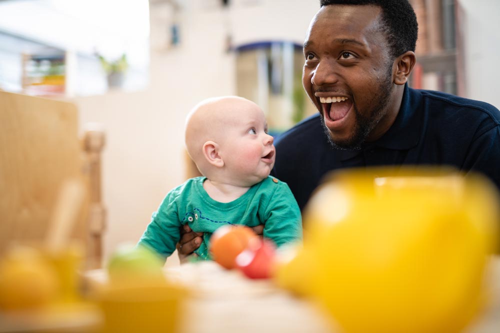 A baby looks at a smiling nursery worker