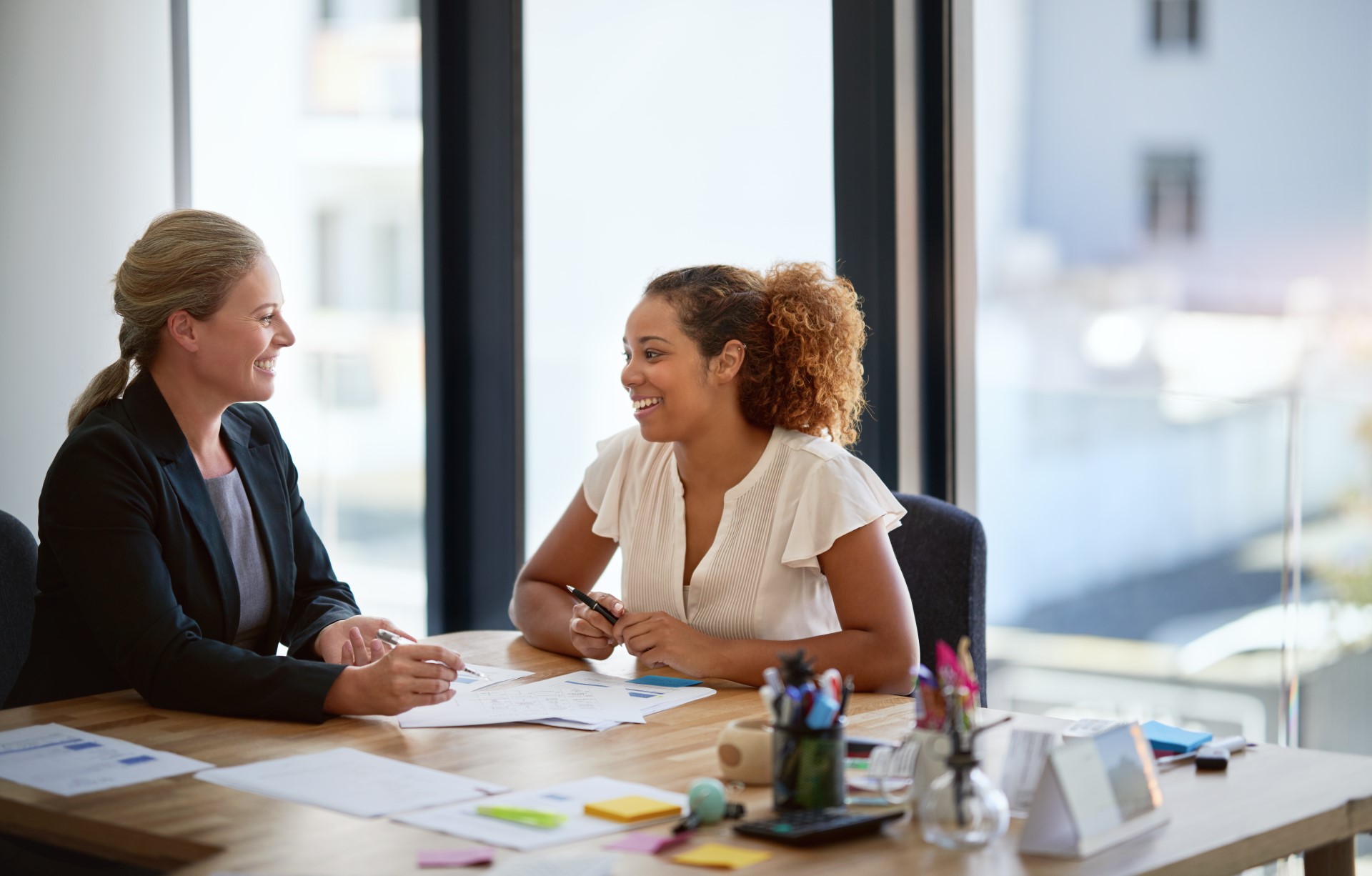 Two smiling businesswoman sitting in an office talking together