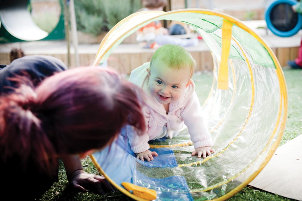 A baby crawls through a tunnel whilst an adult watches