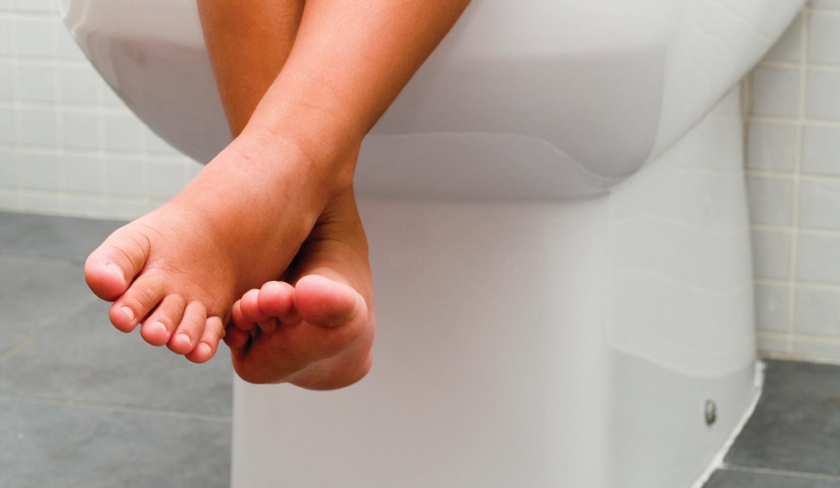 A pair of children's legs dangling from a toilet