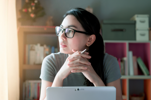 Woman thoughtful about work sitting in front of a laptop at her desk